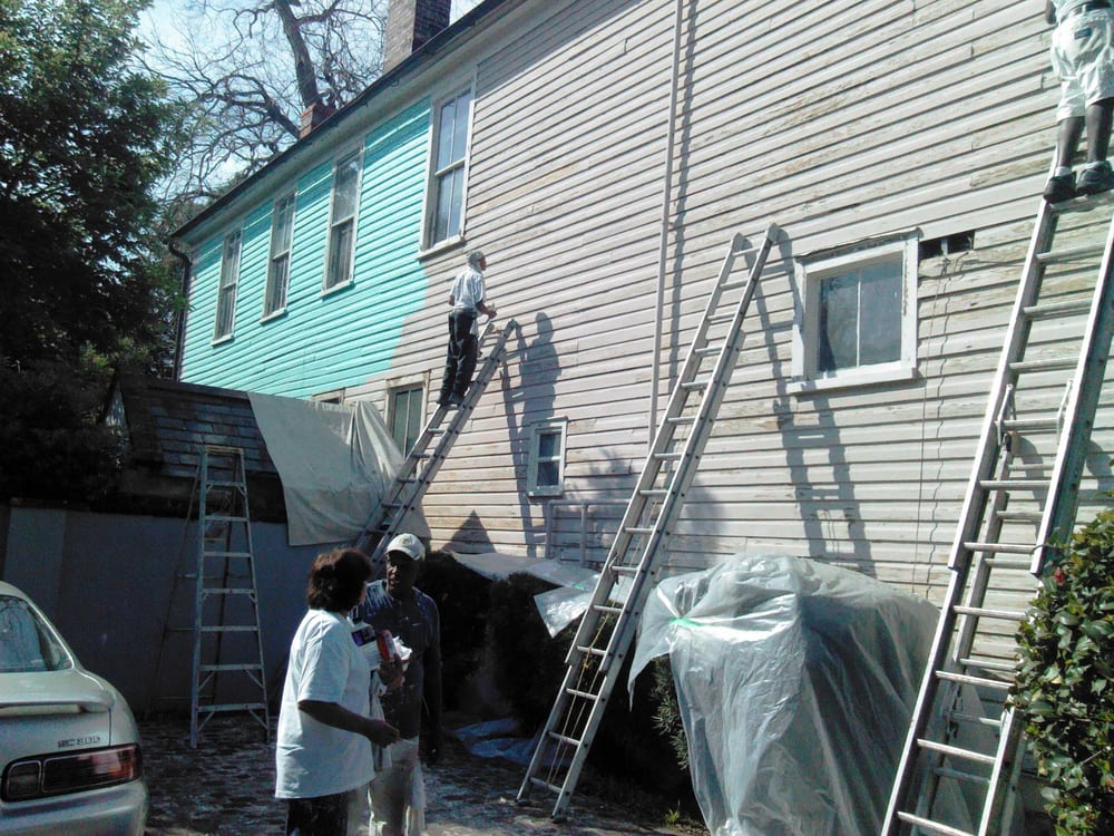 Painters on ladders applying turquoise siding to residential house exterior