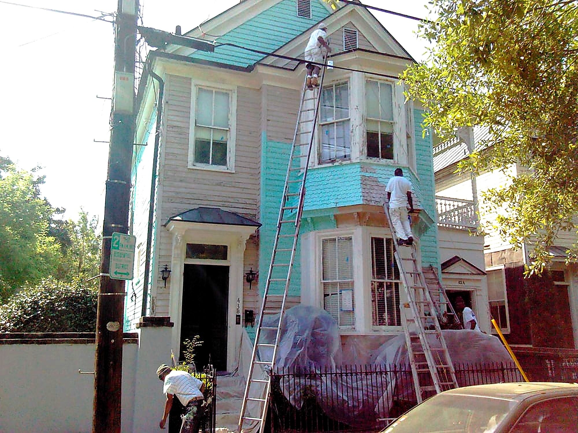 Workers painting turquoise exterior of two-story residential house with ladders